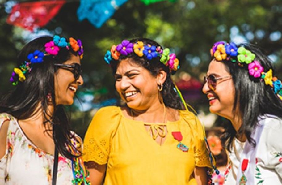 Three Hispanic women wearing bright colored flower crowns, smiling